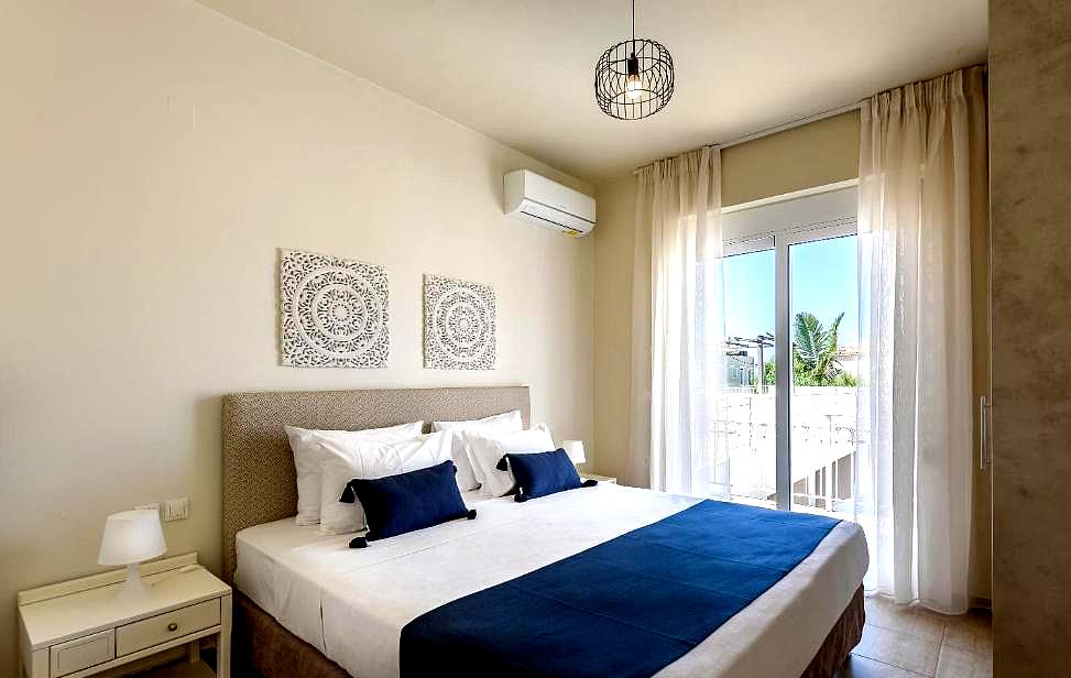 bright bedroom with blue decorative pillows and balcony access with sea view