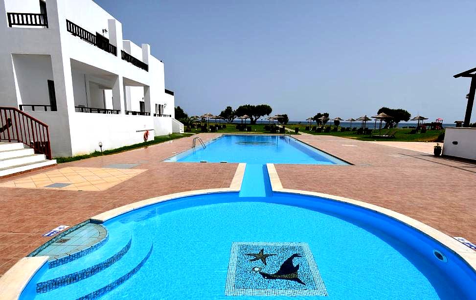 dual swimming pools with dolphin mosaic surrounded by lawn and white buildings with sea view