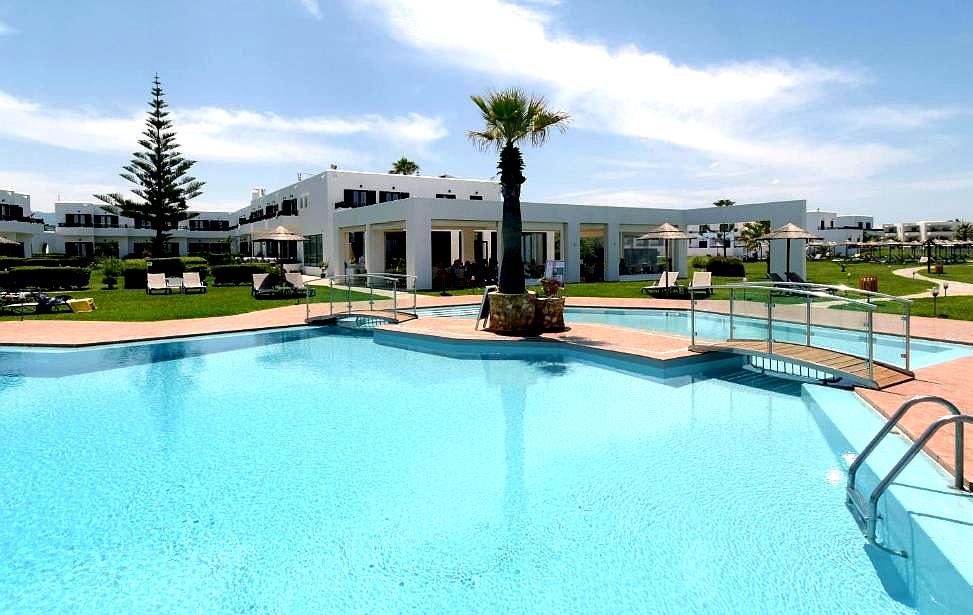 large outdoor swimming pool with bridge surrounded by lawn and white buildings