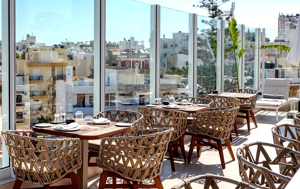 rooftop restaurant with wicker chairs and glass walls overlooking city