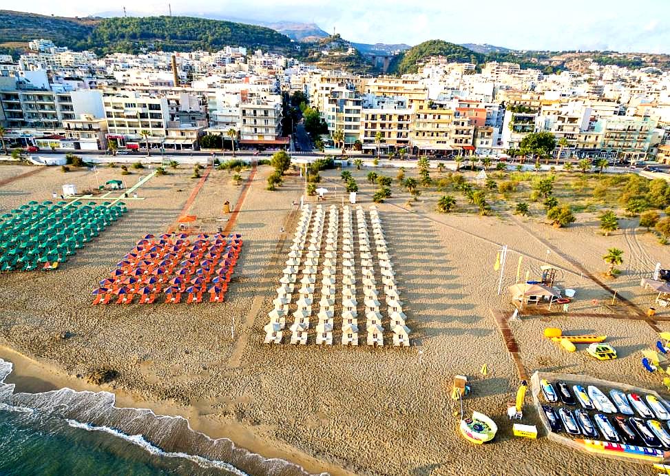 sandy beach with rows of colorful sun loungers and umbrellas