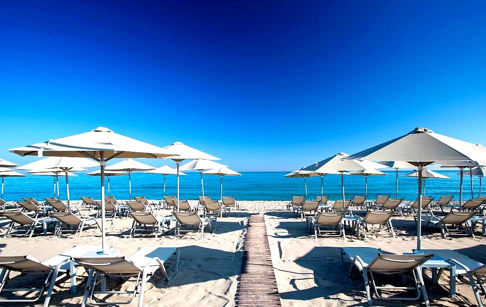 sandy beach with rows of sun loungers and umbrellas facing sea