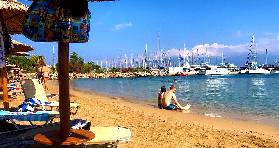 sandy beach with sunbeds near sea and yachts in background